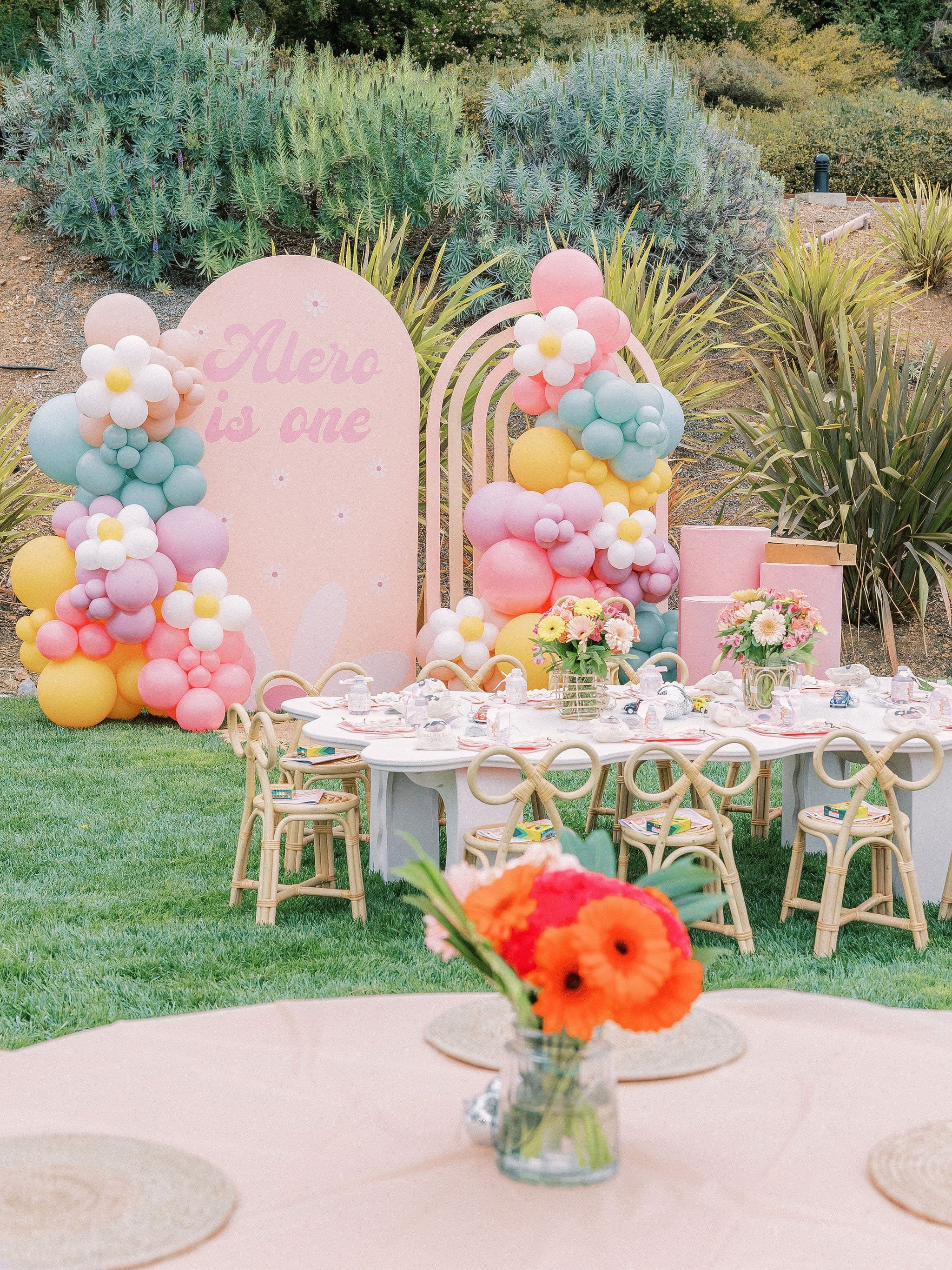 A first birthday party table with a balloon arch on a lawn